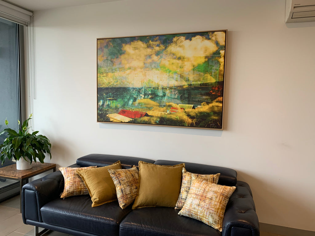 "Bathing in Nostalgia" framed archival canvas print by Durham J White, featuring Mother's Beach, Mornington, with beach huts, swimmers, shifting turquoise blues, light on the water, and a vibrant splash of red, shown box framed in a modern apartment styled with Durham J White Belgian linen cushions in sand and mustard tones.