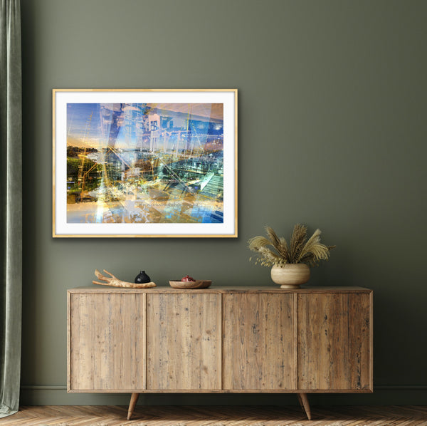 “Keeping Up a Pier Glance 2” glass-framed fine art print by Durham J White, featuring a layered photographic artwork of the Mornington waterfront in luminous pastel blues, subtle lemon highlights, and warm orange accents. Featured in a glass frame in a sage toned living or bedroom space.