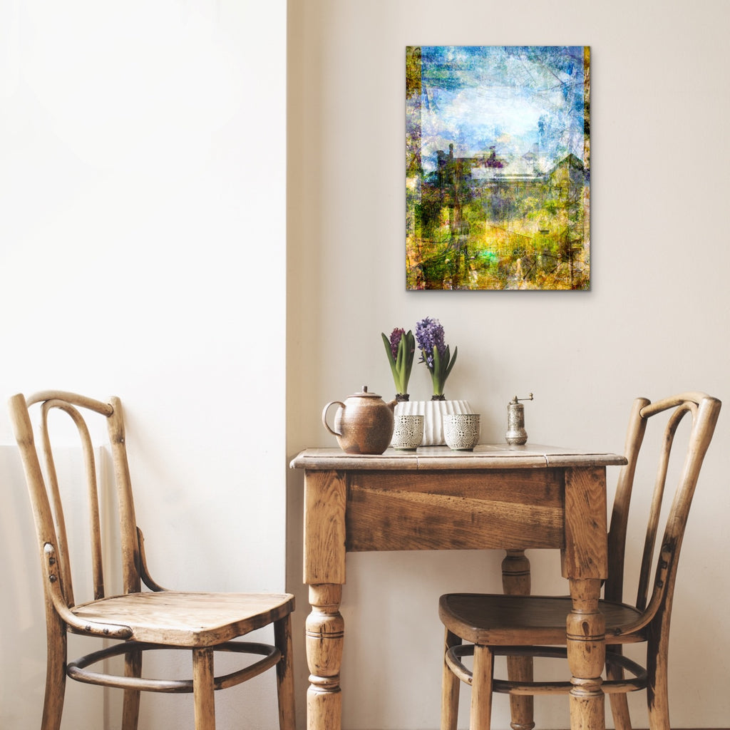 “Quaint” archival canvas print by Durham J White, featuring a layered photographic artwork of Trentham rooftops and chimneys in soft sky blues, crisp whites, and deep garden greens beneath a luminous sky. Small feature piece in a neutral toned cafe.