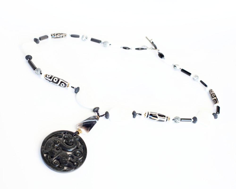 A black and white necklace with a jade dragon like carved pendant.