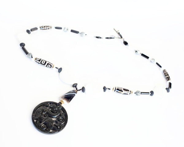A black and white necklace with a jade dragon like carved pendant.
