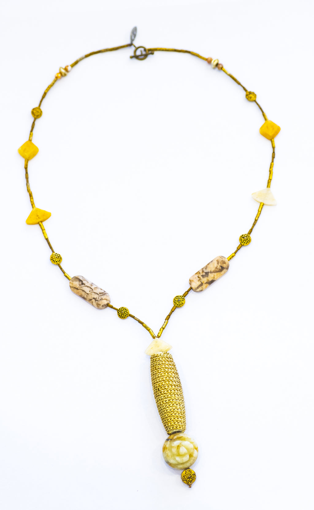 A long, golden necklace with a cylindrical feature and flower carving, displayed against a white background.