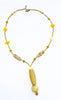 A long, golden necklace with a cylindrical feature and flower carving, displayed against a white background.