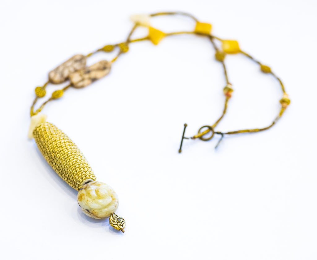 A long, golden necklace with a cylindrical feature and flower carving, displayed against a white background.