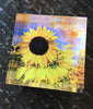 A free-standing decorative art tile featuring a vibrant image of a FleuroSun Classic Gold sunflower with peachy apricot and yellow tones.